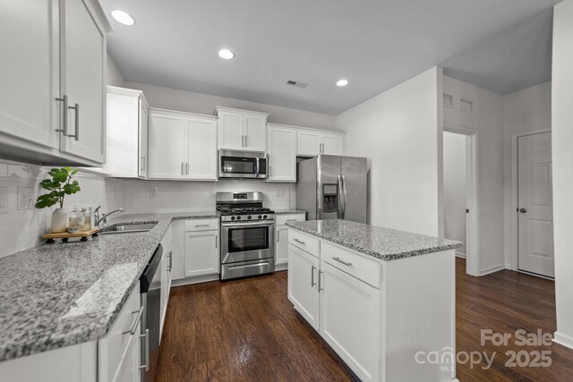 kitchen featuring sink, appliances with stainless steel finishes, a kitchen island, light stone counters, and white cabinetry