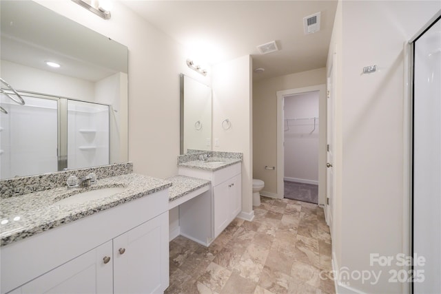 full bathroom with a stall shower, two vanities, a sink, and a walk in closet