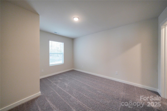 empty room with dark colored carpet, visible vents, and baseboards