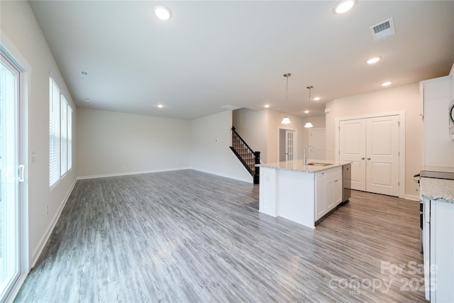 kitchen with a sink, white cabinets, open floor plan, a center island with sink, and decorative light fixtures