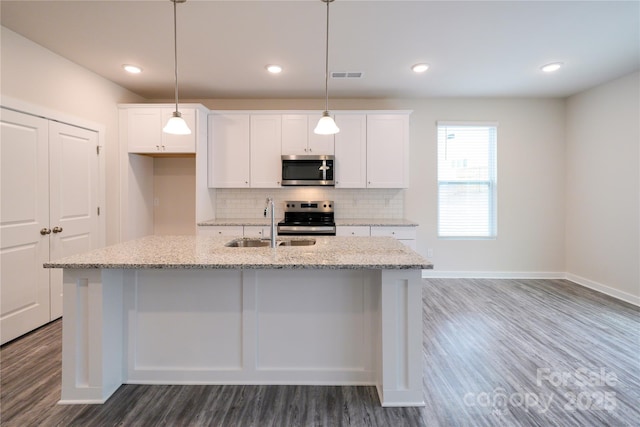 kitchen featuring light stone counters, appliances with stainless steel finishes, and a kitchen island with sink