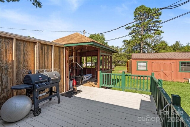 wooden terrace featuring a yard, an outbuilding, and a grill