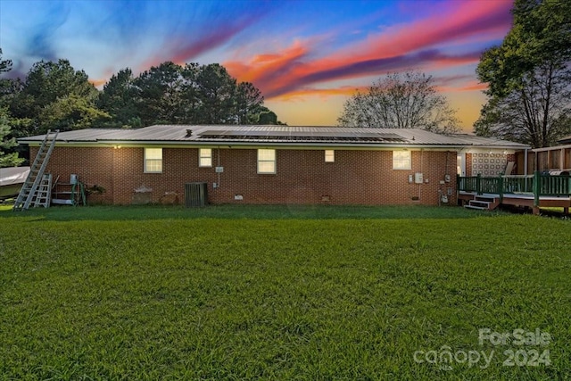 back house at dusk with central AC, a wooden deck, and a lawn