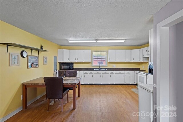 kitchen featuring sink, light wood-type flooring, a textured ceiling, exhaust hood, and white cabinetry