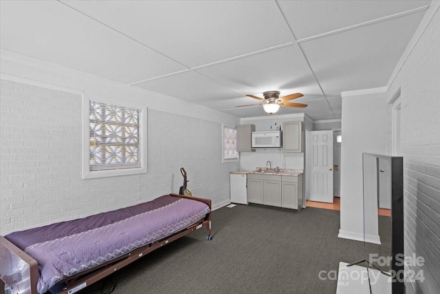 bedroom with a ceiling fan, brick wall, crown molding, dark carpet, and a sink