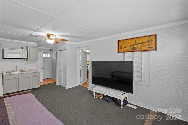 living area with ceiling fan, brick wall, ornamental molding, and dark colored carpet