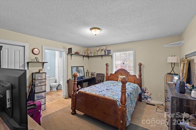 bedroom featuring light colored carpet, a closet, ensuite bathroom, and a textured ceiling