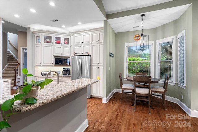 kitchen with a notable chandelier, appliances with stainless steel finishes, light stone countertops, wood-type flooring, and decorative backsplash