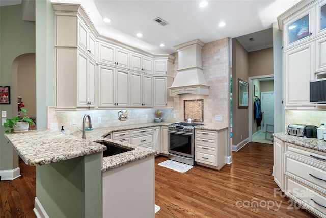 kitchen with stainless steel range with gas cooktop, hardwood / wood-style floors, kitchen peninsula, and premium range hood