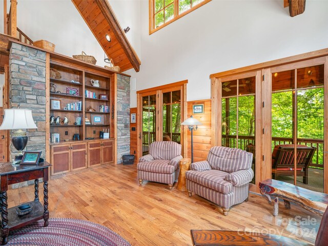 interior space with wood walls, beamed ceiling, high vaulted ceiling, and light hardwood / wood-style floors