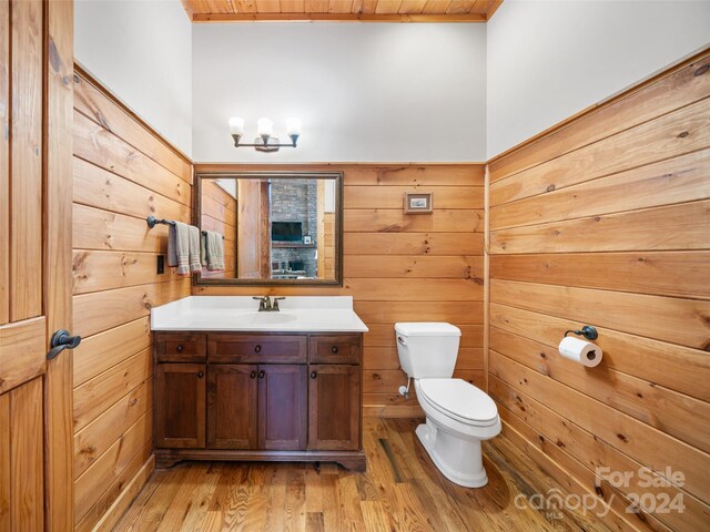 bathroom featuring toilet, wooden walls, vanity, wood-type flooring, and wood ceiling