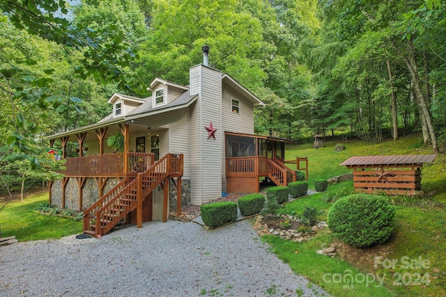 exterior space featuring a sunroom, a chimney, stairs, a deck, and a front lawn