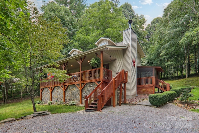 view of front of property with a sunroom, stone siding, a chimney, stairs, and a front yard