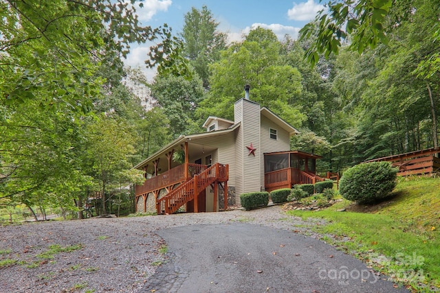 view of front of property featuring stairs, a chimney, a wooden deck, and a sunroom