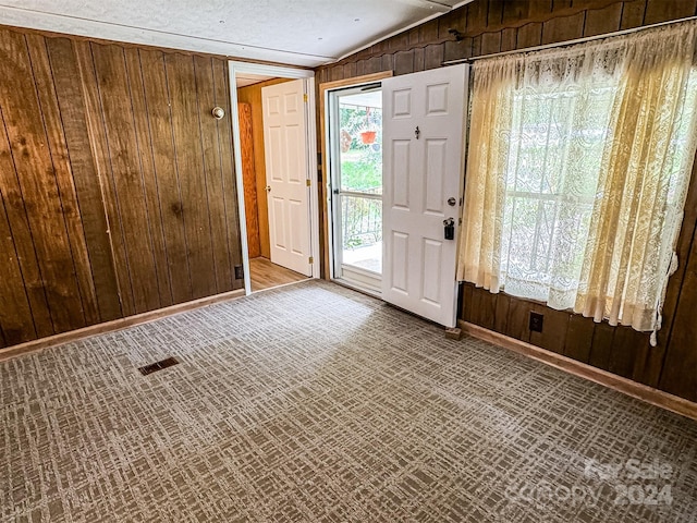 entrance foyer featuring a wealth of natural light, vaulted ceiling, and wood walls