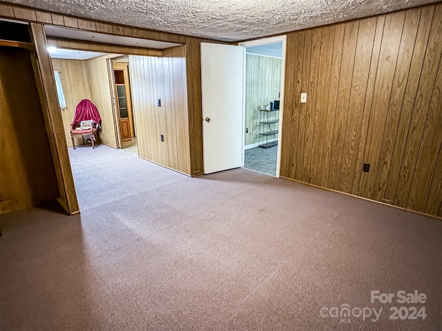 carpeted spare room featuring wooden walls and a textured ceiling