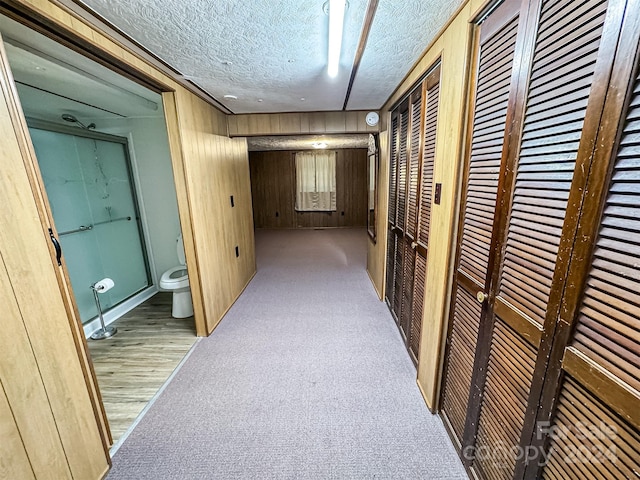 hall with carpet flooring, a textured ceiling, and wood walls