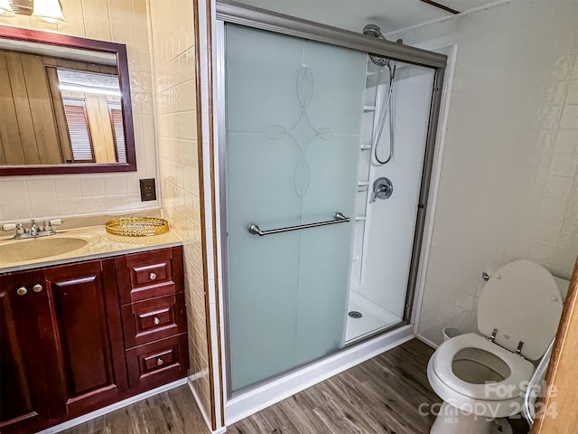 bathroom featuring hardwood / wood-style flooring, a shower with shower door, vanity, tile walls, and toilet