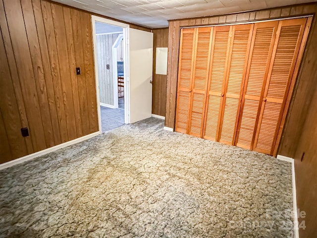 unfurnished bedroom featuring wood walls, a closet, and carpet flooring