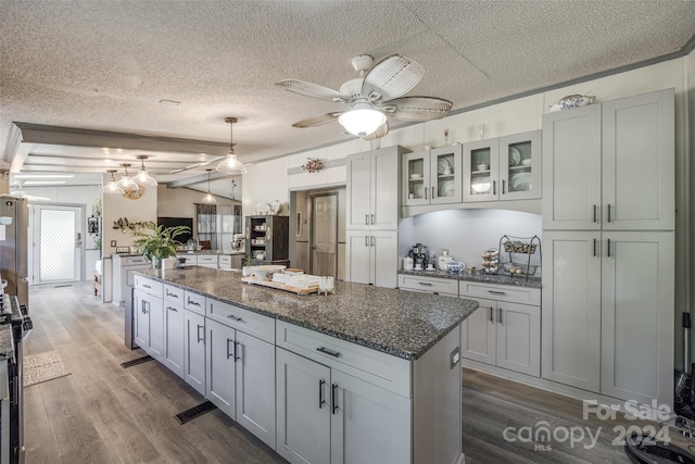 kitchen with a textured ceiling, wood-type flooring, dark stone counters, a center island, and decorative light fixtures