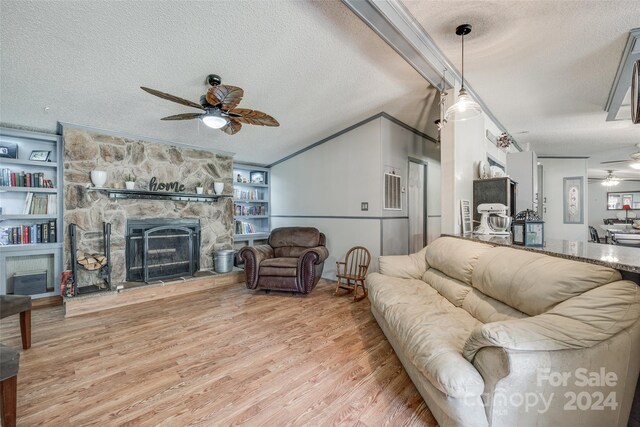 living room featuring hardwood / wood-style floors, ceiling fan, a textured ceiling, ornamental molding, and a stone fireplace