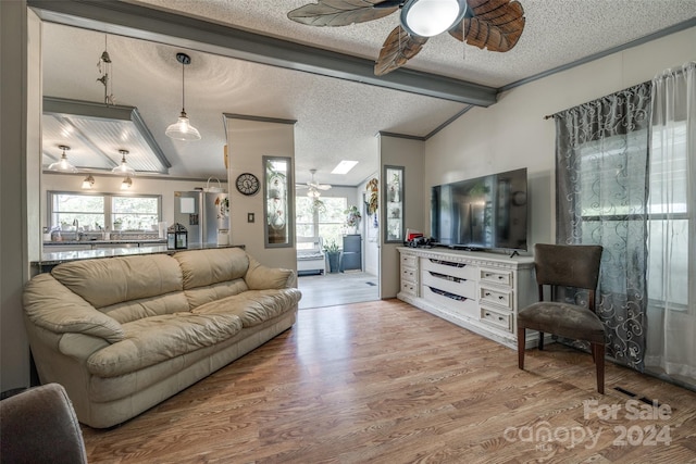 living room with light hardwood / wood-style floors, lofted ceiling with skylight, a textured ceiling, and ceiling fan