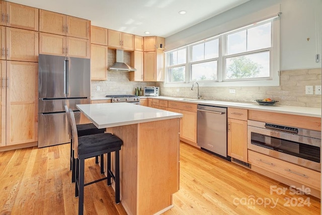 kitchen featuring wall chimney range hood, stainless steel appliances, a center island, a breakfast bar area, and light wood-type flooring