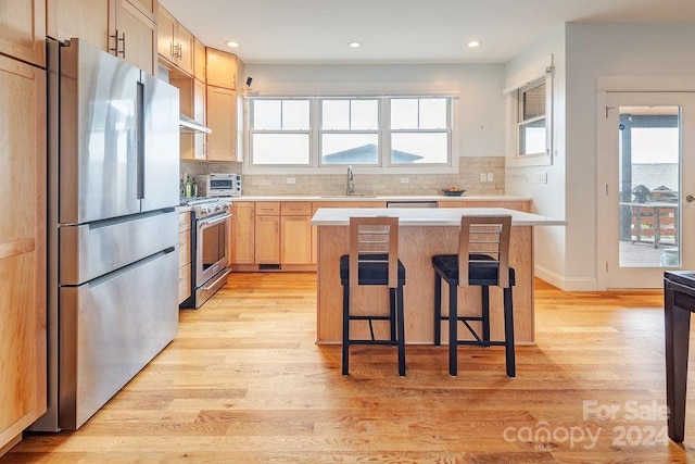 kitchen featuring light wood-type flooring, a kitchen island, a kitchen breakfast bar, stainless steel appliances, and light brown cabinets