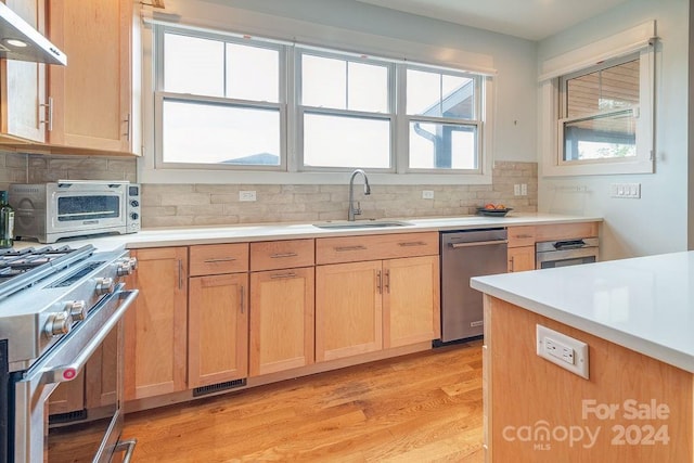 kitchen with tasteful backsplash, sink, light hardwood / wood-style flooring, appliances with stainless steel finishes, and extractor fan