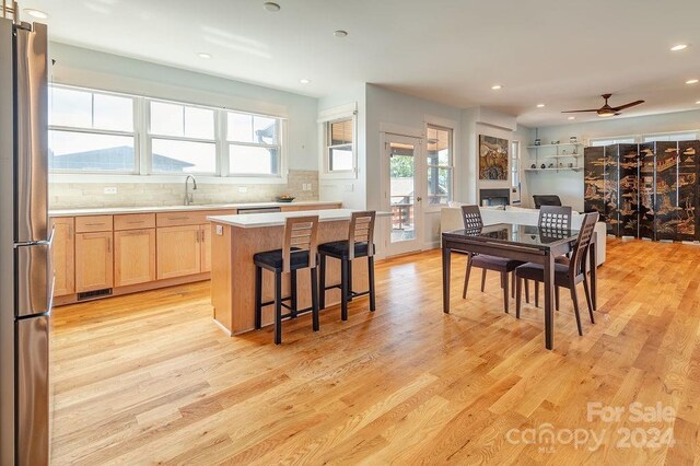 kitchen featuring stainless steel refrigerator, a kitchen island, light wood-type flooring, ceiling fan, and sink