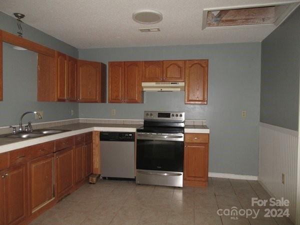 kitchen with appliances with stainless steel finishes, sink, light tile patterned floors, and a textured ceiling