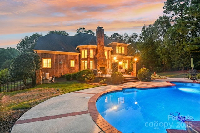 pool at dusk with a patio area and a yard