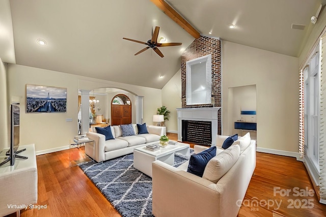 living room with ornate columns, ceiling fan, hardwood / wood-style flooring, a fireplace, and vaulted ceiling with beams