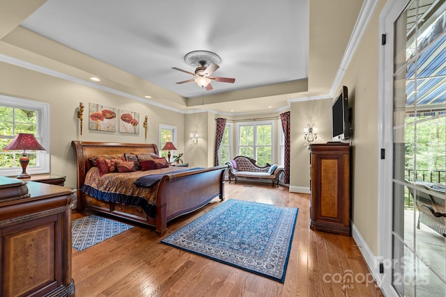 bedroom featuring ceiling fan, a raised ceiling, light wood-type flooring, and crown molding