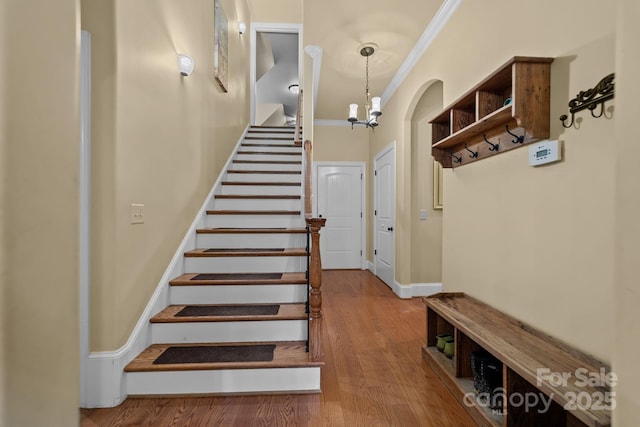 staircase with hardwood / wood-style flooring, crown molding, and a notable chandelier