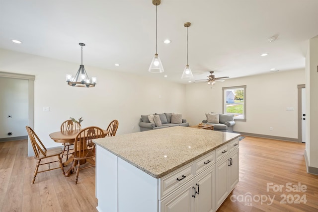 kitchen featuring light stone counters, hanging light fixtures, open floor plan, white cabinetry, and light wood-type flooring