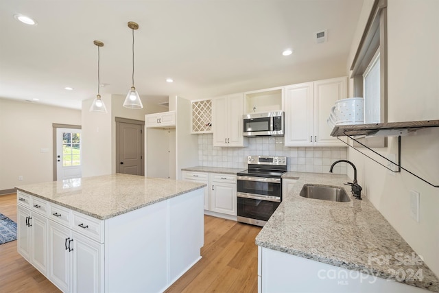 kitchen featuring hanging light fixtures, light stone counters, stainless steel appliances, and a sink