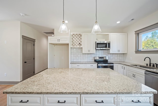 kitchen with a kitchen island, light stone counters, decorative light fixtures, stainless steel appliances, and a sink