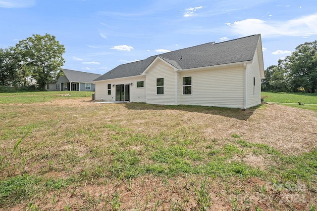 rear view of house with roof with shingles and a lawn