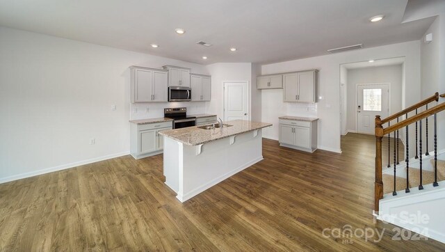 kitchen with appliances with stainless steel finishes, hardwood / wood-style flooring, a center island with sink, tasteful backsplash, and sink