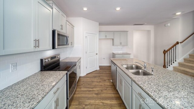 kitchen featuring dark hardwood / wood-style floors, appliances with stainless steel finishes, sink, tasteful backsplash, and light stone counters