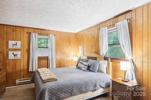 bedroom featuring a baseboard radiator, dark hardwood / wood-style flooring, wooden walls, and a textured ceiling