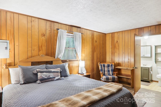 bedroom featuring connected bathroom, a textured ceiling, and wood walls