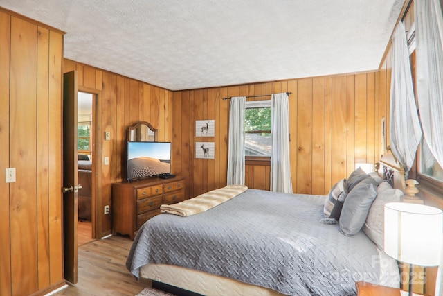 bedroom with wooden walls, a textured ceiling, and light hardwood / wood-style flooring