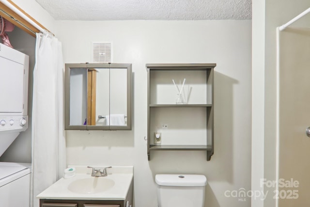 bathroom with stacked washing maching and dryer, vanity, a textured ceiling, curtained shower, and toilet