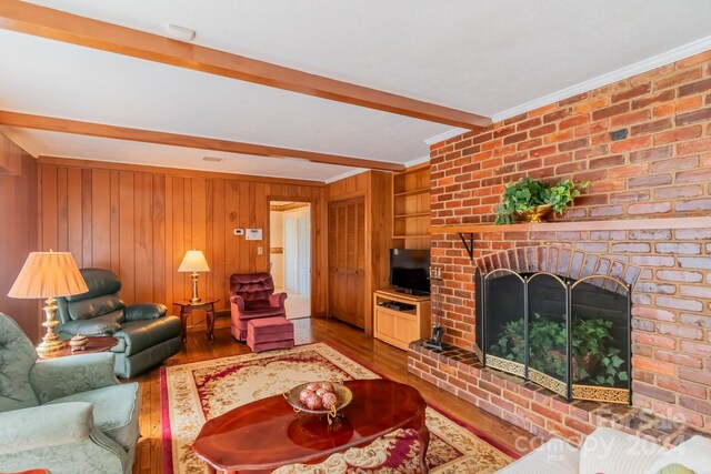 living room with wood walls, beam ceiling, brick wall, hardwood / wood-style flooring, and a brick fireplace