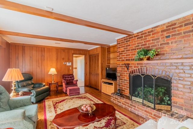 living room featuring wooden walls, wood finished floors, built in features, ornamental molding, and beam ceiling