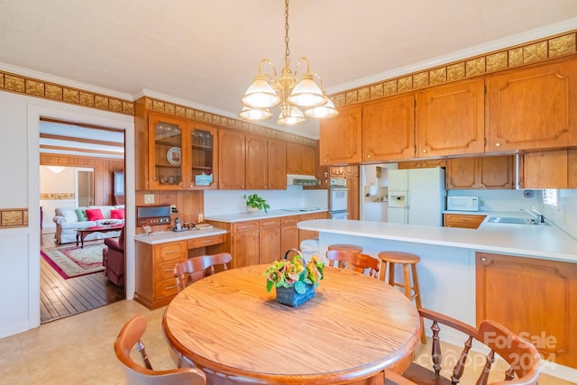 kitchen with a notable chandelier, light hardwood / wood-style flooring, white appliances, crown molding, and pendant lighting