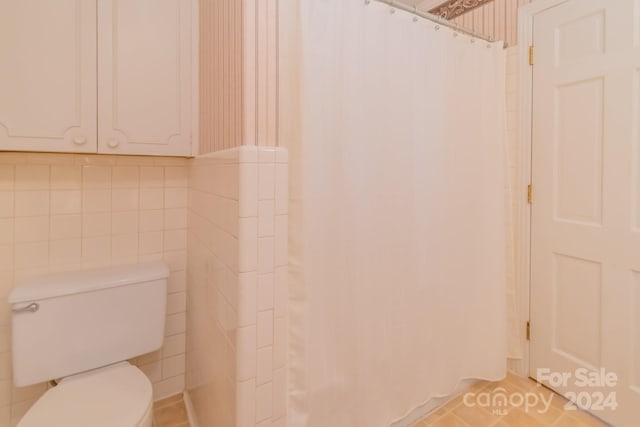 bathroom with a shower with shower curtain, toilet, tile patterned flooring, and tile walls