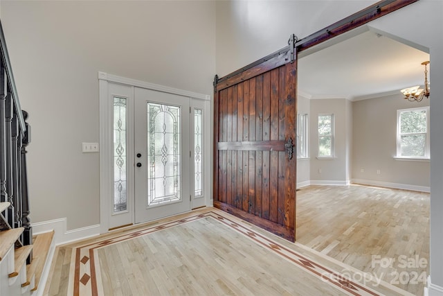 entryway featuring a barn door, light wood-type flooring, ornamental molding, and an inviting chandelier